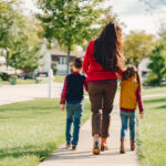 Moeder wandelt met twee kinderen over trottoir in groene gezinsvriendelijke wijk