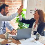 Twee collega&rsquo;s geven elkaar een high five na een succesvolle samenwerking met een online bureau kiezen als thema.