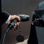 Man in pak sluit laadpaal aan op elektrische auto, symbool voor laadpaal in appartementencomplex.