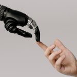 Menselijke hand raakt vingertop van robotarm aan, symbolisch voor samenwerking met een AI-assistent.