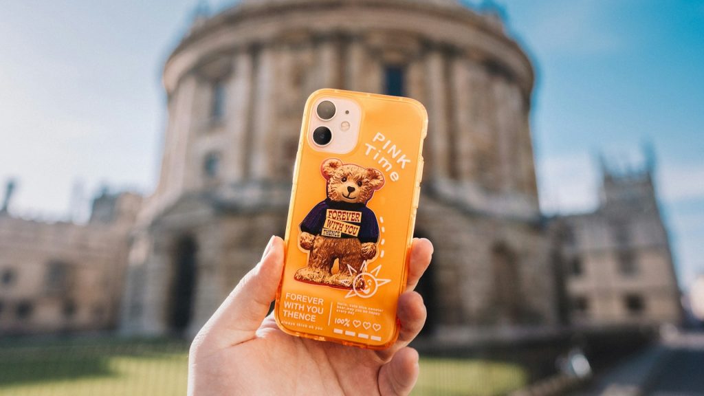 Gepersonaliseerd telefoonhoesje met teddybeerontwerp dat in de hand wordt gehouden voor een historisch gebouw